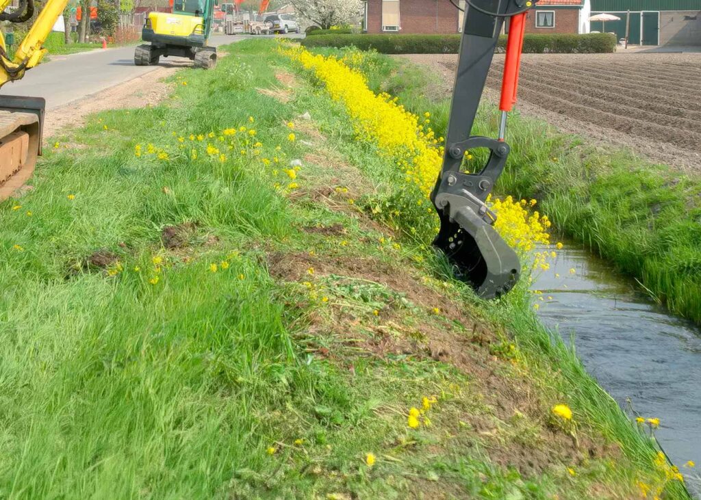 Escavatore con braccio prolunga al lavoro nella pulizia di un fosso lungo un canale.