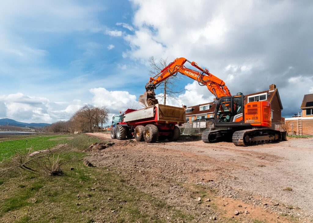 Escavatore cingolato carica terra su un camion ribaltabile durante lavori in cantiere.