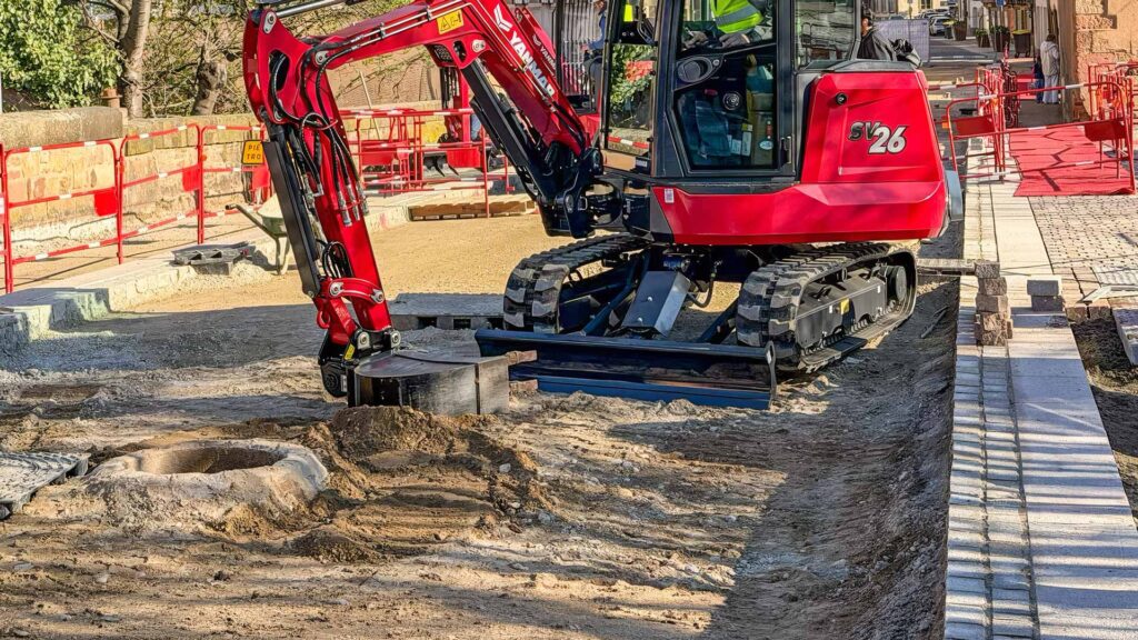 Miniescavatore Yanmar SV26 con cingoli in gomma impegnato in lavori urbani su superficie pavimentata.