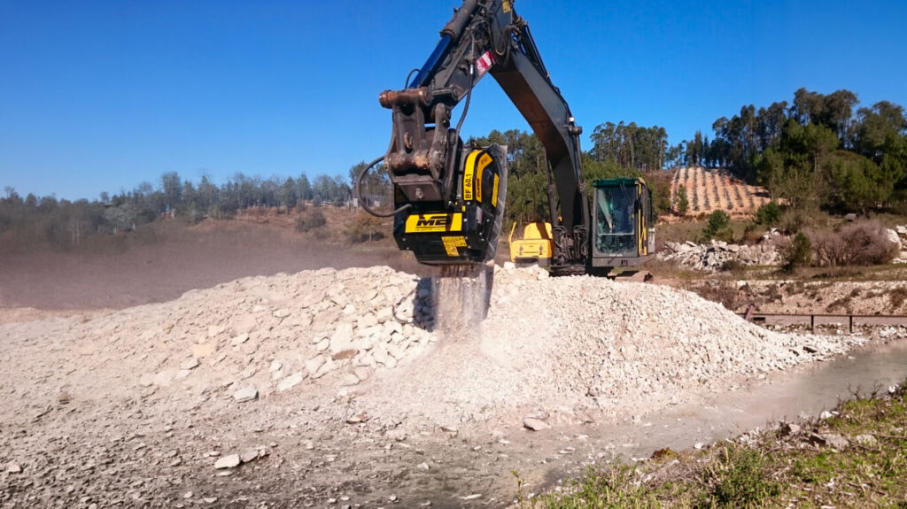 Benna frantoio montata su escavatore durante la frantumazione in loco di materiale da demolizione per il riutilizzo in cantiere.
