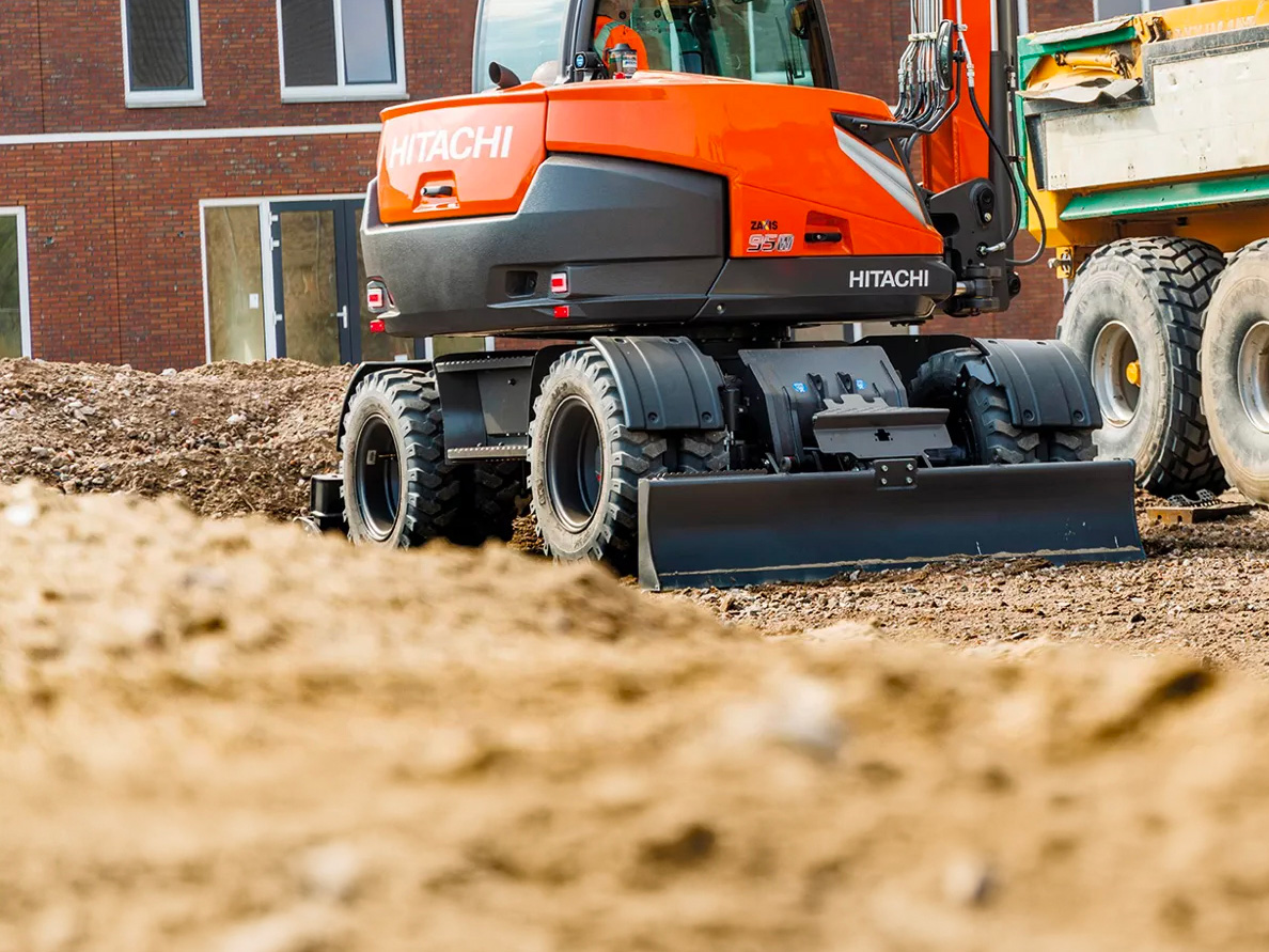 Escavatore gommato Hitachi impegnato in un cantiere urbano durante lavori di movimento terra su strada.